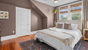 A bedroom with a sloped ceiling, a bed with white bedding, a ceiling fan, and a window with blinds. - Updated, Historic District, Walk to Waterfront. Pet-Friendly! Sleeps 12 (Warren)