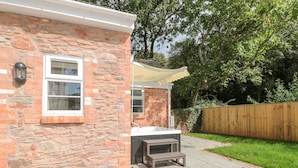 A stone building with a window, a wooden bench, and a patio area. - The Nest (Bridgwater)