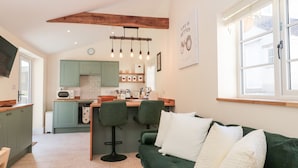 A cozy living room with a green sofa and a kitchen area in the background. - The Nest (Bridgwater)