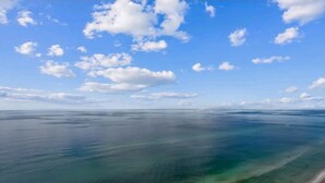 A wide view of a calm sea under a clear sky with scattered clouds.