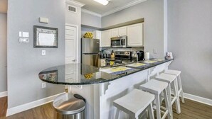A modern kitchen with a central island, white cabinetry, stainless steel appliances, and bar stools.