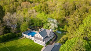 Une grande maison avec une piscine, entourée d’une végétation luxuriante et située dans un paysage vallonné.