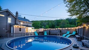 Un jardin avec une piscine, des chaises longues et des guirlandes lumineuses.