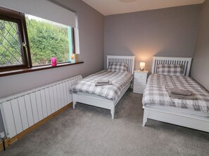 A bedroom with two beds, a window, a bedside table with a lamp, and a radiator. - Drumore House (Laddan)