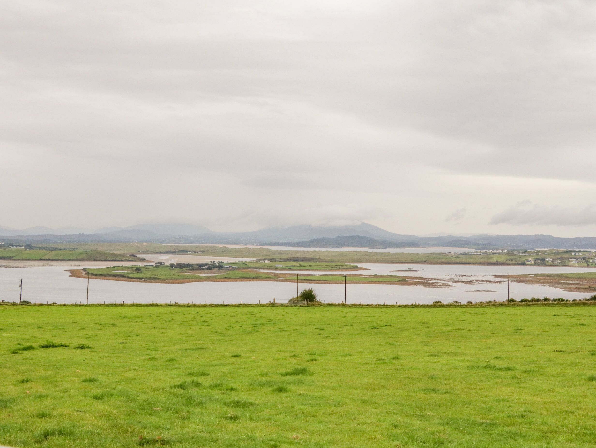 A grassy field with a river and distant mountains.