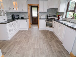 A modern kitchen with white cabinets, a central island, and a built-in oven. - Drumore House (Laddan)