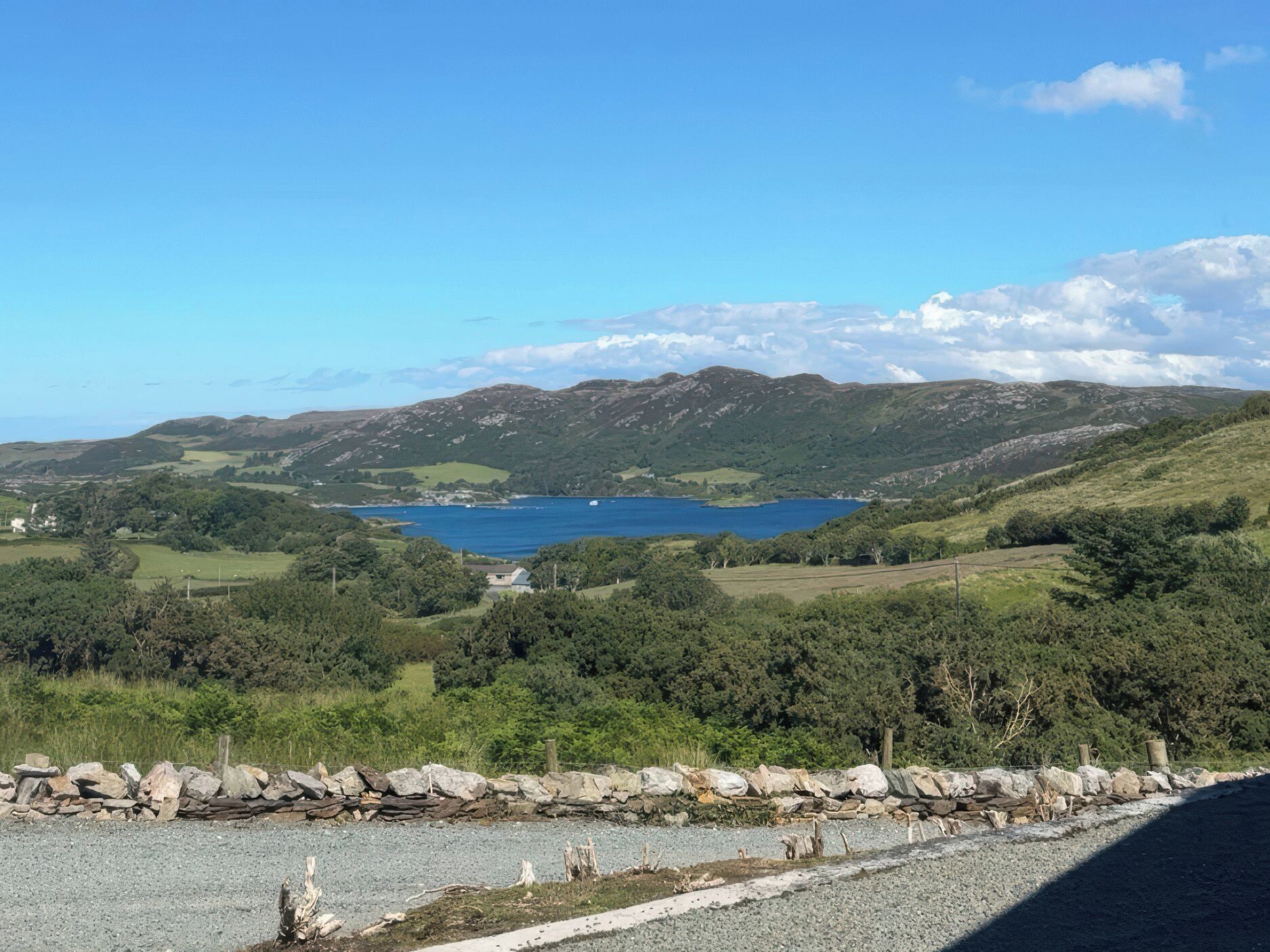 Paisatge costaner amb una vista clara d'un llac, turons ondulats i una paret de pedra al primer terme.
