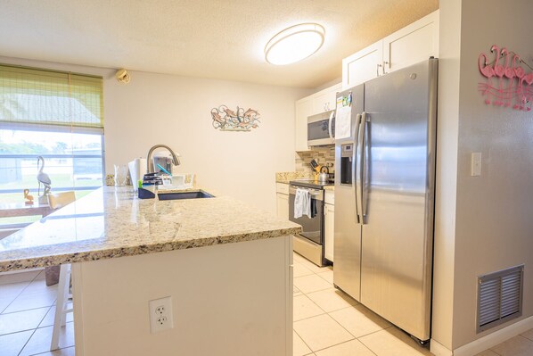 A kitchen with a granite countertop, stainless steel appliances, a microwave, and a refrigerator.