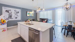A modern kitchen with a central island, stainless steel appliances, pendant lighting, and a dining area with a table and chairs. - Themed Townhome near Parks and Much More! (Davenport)