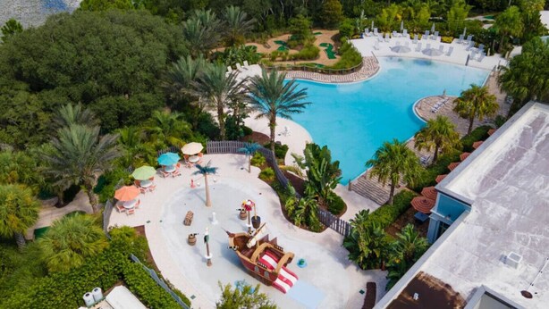 An aerial view of a resort with a large swimming pool, palm trees, and outdoor seating areas. - Themed Townhome near Parks and Much More! (Davenport)