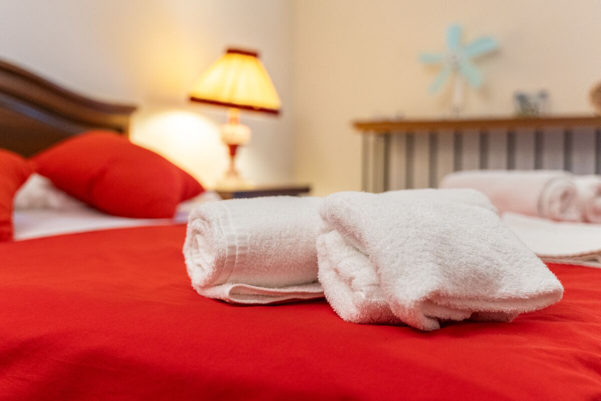 Un lit bien fait, avec une literie rouge et des serviettes blanches, une lampe et une jolie hélice bleue décorative accrochée au mur.