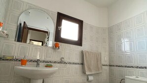 Un baño con lavamanos, espejo, inodoro y un pequeño taburete de madera.
