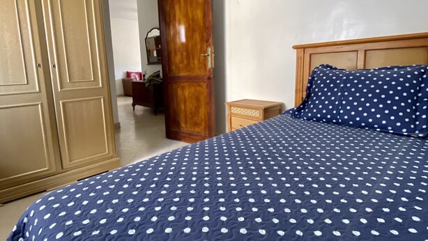 Un dormitorio con una cama cubierta por un edredón de lunares, un armario de madera y una puerta de madera.