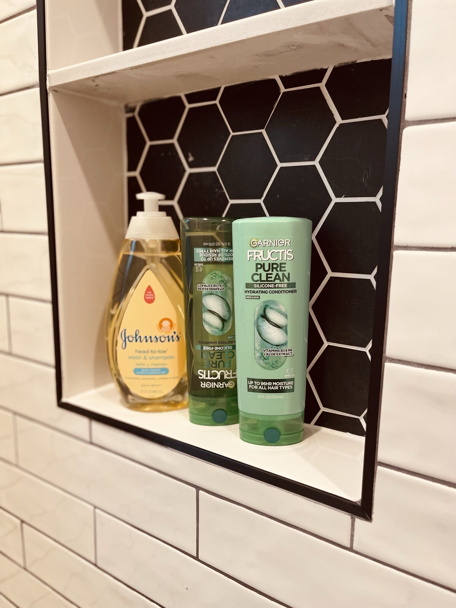 A bathroom shelf with three bottles of hair care products.