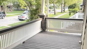 A covered porch with a wooden floor and white railings.