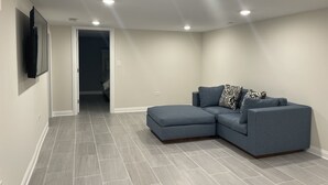 Ein modernes Wohnzimmer mit Ecksofa, Einbauleuchten und einem flachbildfernseher an der Wand.