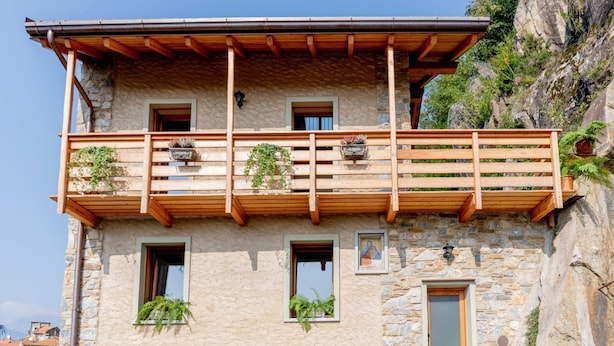 A stone building with a wooden balcony, multiple windows, and potted plants.