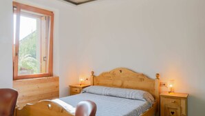 A single bed with a wooden headboard, two bedside tables with lamps, and a window with a view of greenery.
