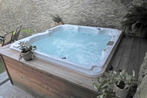 A hot tub on a wooden deck with a stone wall in the background.