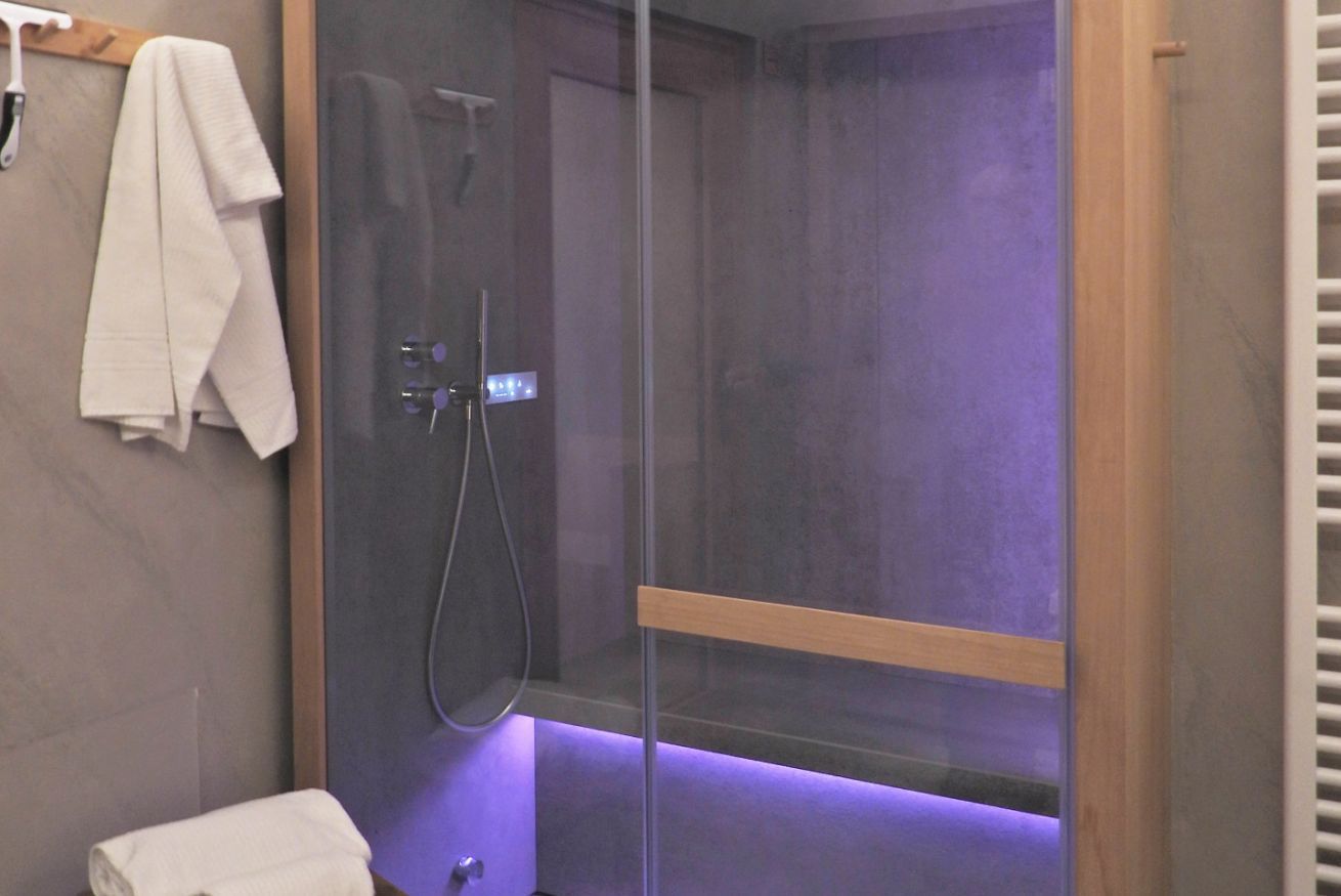 A modern bathroom with a glass-enclosed shower, a wooden shelf, and a white towel on the wall.