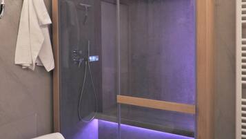 A modern bathroom with a glass-enclosed shower, a wooden shelf, and a white towel on the wall.