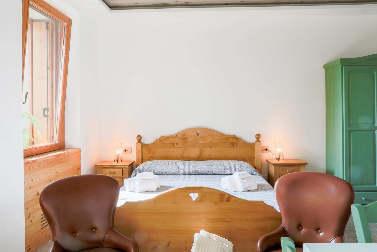 Un dormitorio con una cama de madera, dos mesitas de noche con lámparas, un armario verde y una ventana con vistas.