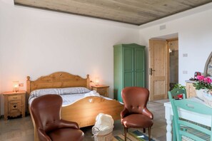 Un dormitorio con una cama de madera, dos sillas marrones, un armario verde y una mesa blanca con un cesto de flores.