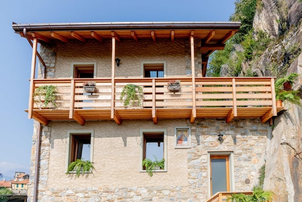 A stone building with a wooden balcony, multiple windows, and potted plants.