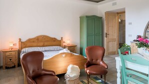 A bedroom with a wooden bed, two brown chairs, a green wardrobe, and a white table with a basket of flowers.