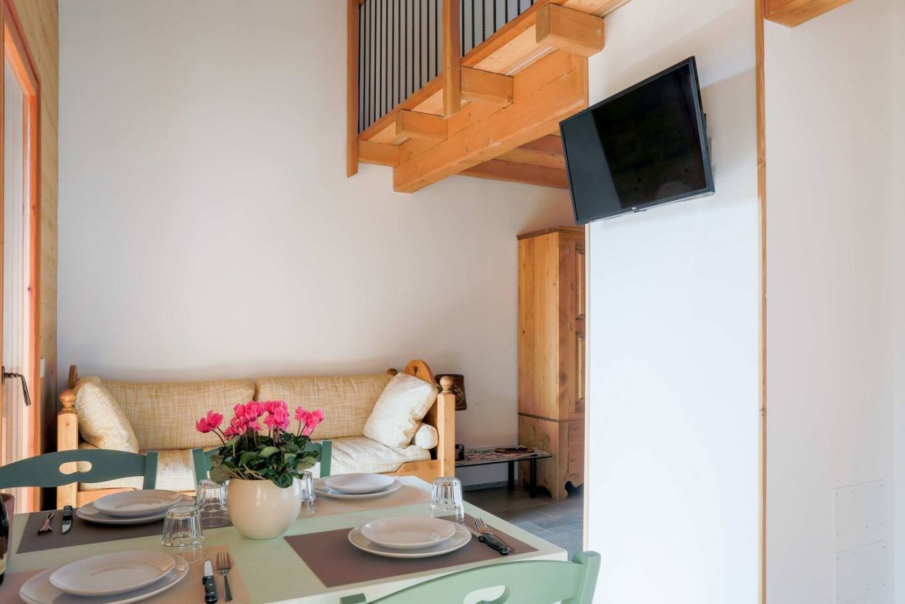 Un coin repas avec une table dressée pour quatre personnes, un canapé et un téléviseur fixé au mur.