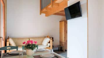 Un coin repas avec une table dressée pour quatre personnes, un canapé et un téléviseur fixé au mur.