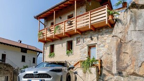 A stone building with a balcony, a parked car, and a stone wall. - Green Chalet Scalotta - private Jacuzzi and SPA - few steps from lake and best trekking (Dervio)