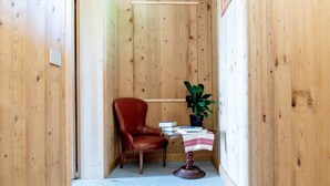 A narrow hallway with wooden walls, a red leather chair, a small table with a plant, and a few books. - Green Chalet Scalotta - private Jacuzzi and SPA - few steps from lake and best trekking (Dervio)