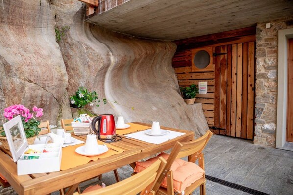 Une table de salle à manger en bois, dressée avec de l’assiette blanche, des tasses et une bouilloire rouge, entourée de chaises dotées de coussins couleur pêche.