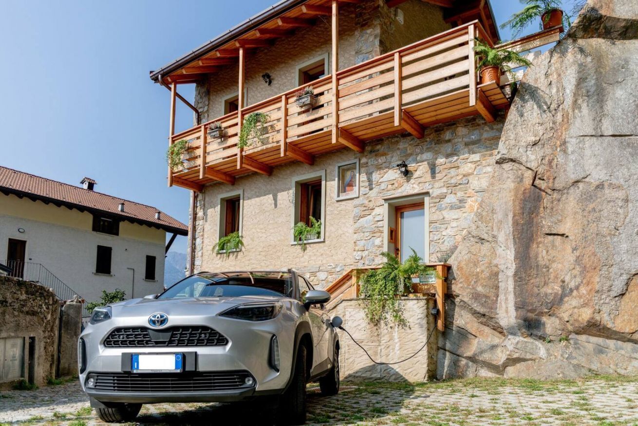 Ein Steinhaus mit Balkon, einem geparkten Auto und einer Steinmauer.