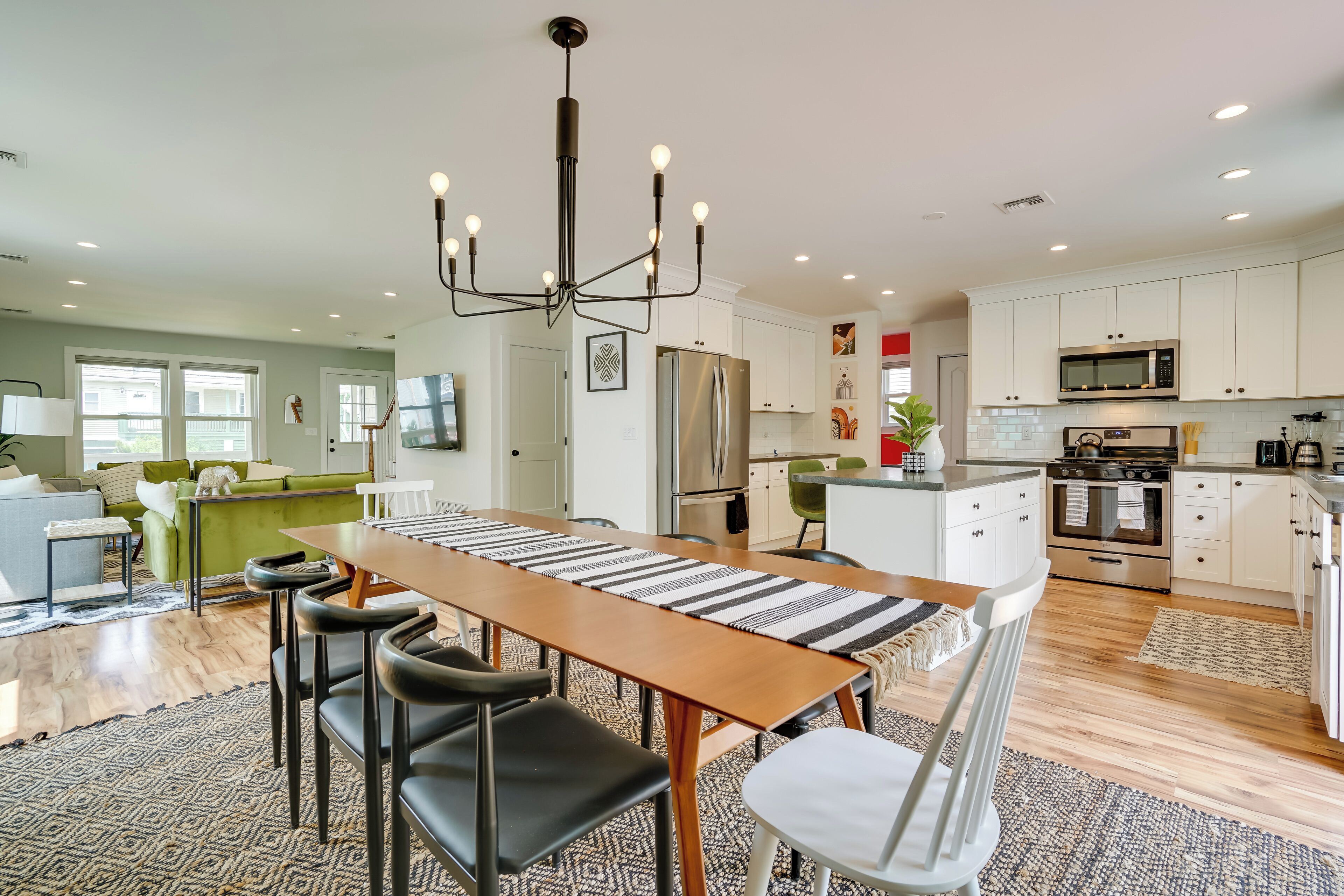 A spacious kitchen with modern appliances, a dining area with a long table and chairs, and a cozy living area with a green sofa.