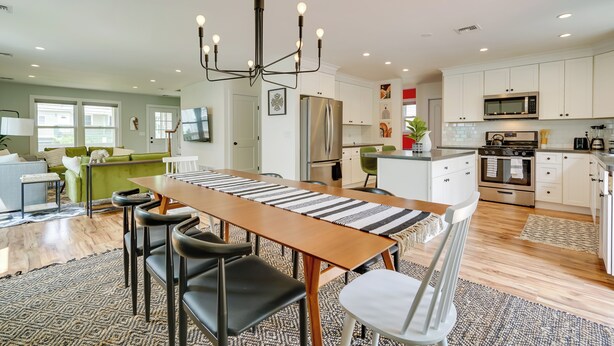 Une cuisine spacieuse équipée d’appareils modernes, un coin repas avec une longue table et des chaises, et un salon confortable avec un canapé vert.