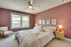 Une chambre à coucher avec un grand lit, une chaise blanche, une table de chevet avec une lampe et un ventilateur de plafond.