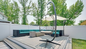 Une terrasse en bois avec un canapé et un fauteuil suspendu.