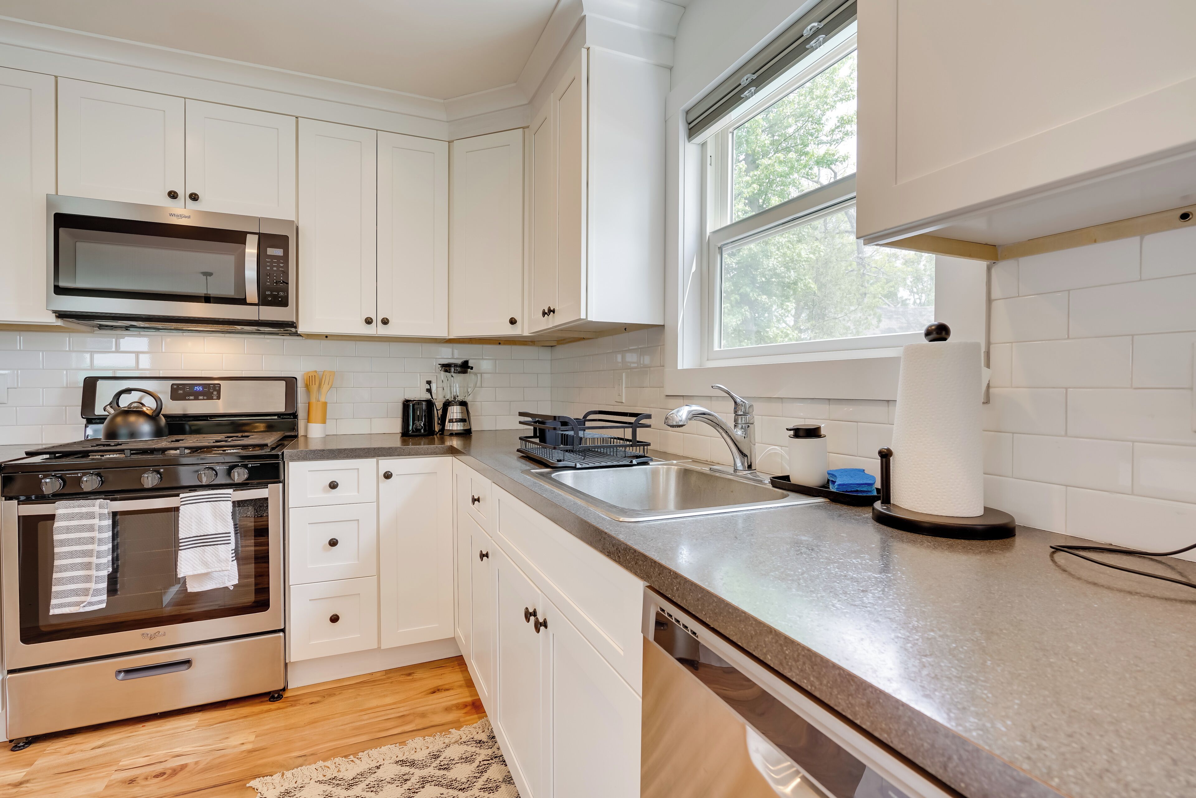 A modern kitchen with white cabinets, stainless steel appliances, and a large window providing natural light.