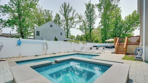 Une piscine rectangulaire dotée d’une terrasse blanche, entourée d’une clôture blanche et d’arbres.