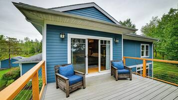 A blue house with a deck featuring two wooden chairs with blue cushions.