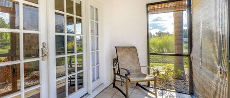 A covered patio with a chair, a sliding glass door, and a view of the garden.