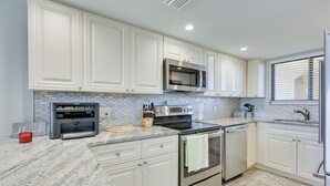 A kitchen with white cabinets, a granite countertop, stainless steel appliances, and a tiled backsplash. - Gulf-view Balcony & Pool Access: Hudson Retreat (Hudson)