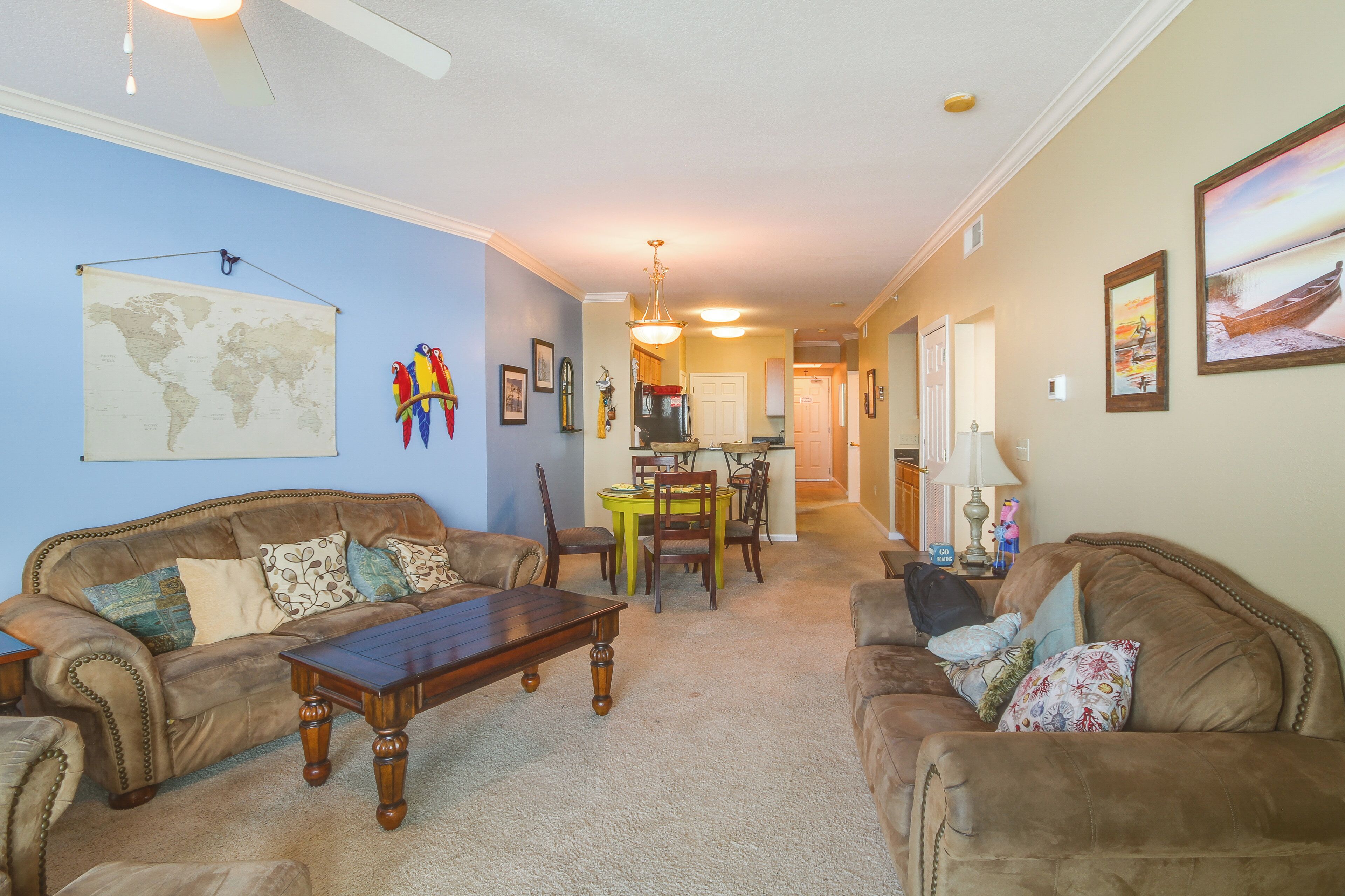 A living room with two sofas, a coffee table, and a dining table with chairs. There is a world map on the wall and a painting.