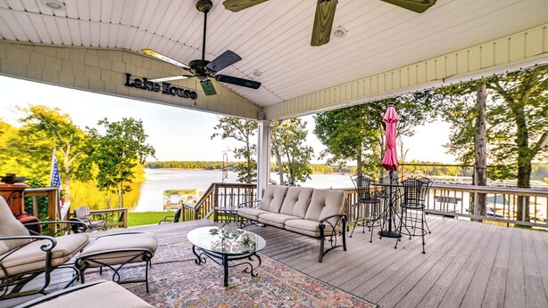 A covered outdoor deck with a sofa, chairs, a table, and a ceiling fan. - Pet-friendly New Concord Vacation Rental on Lake! (New Concord)