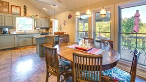 A spacious kitchen with wooden cabinets, a dining table with chairs, and a large window overlooking a deck. - Pet-friendly New Concord Vacation Rental on Lake! (New Concord)
