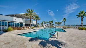A swimming pool with a sunshade, palm trees, and a modern building with large windows. - Luxe Resort Condo - 2 Mi to Daytona Beach! (Holly Hill)