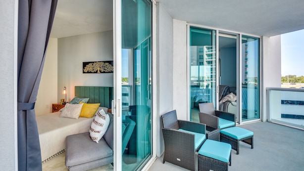 A balcony with wicker furniture and a sliding glass door leading to a room with a bed and a nightstand. - Luxe Resort Condo - 2 Mi to Daytona Beach! (Holly Hill)
