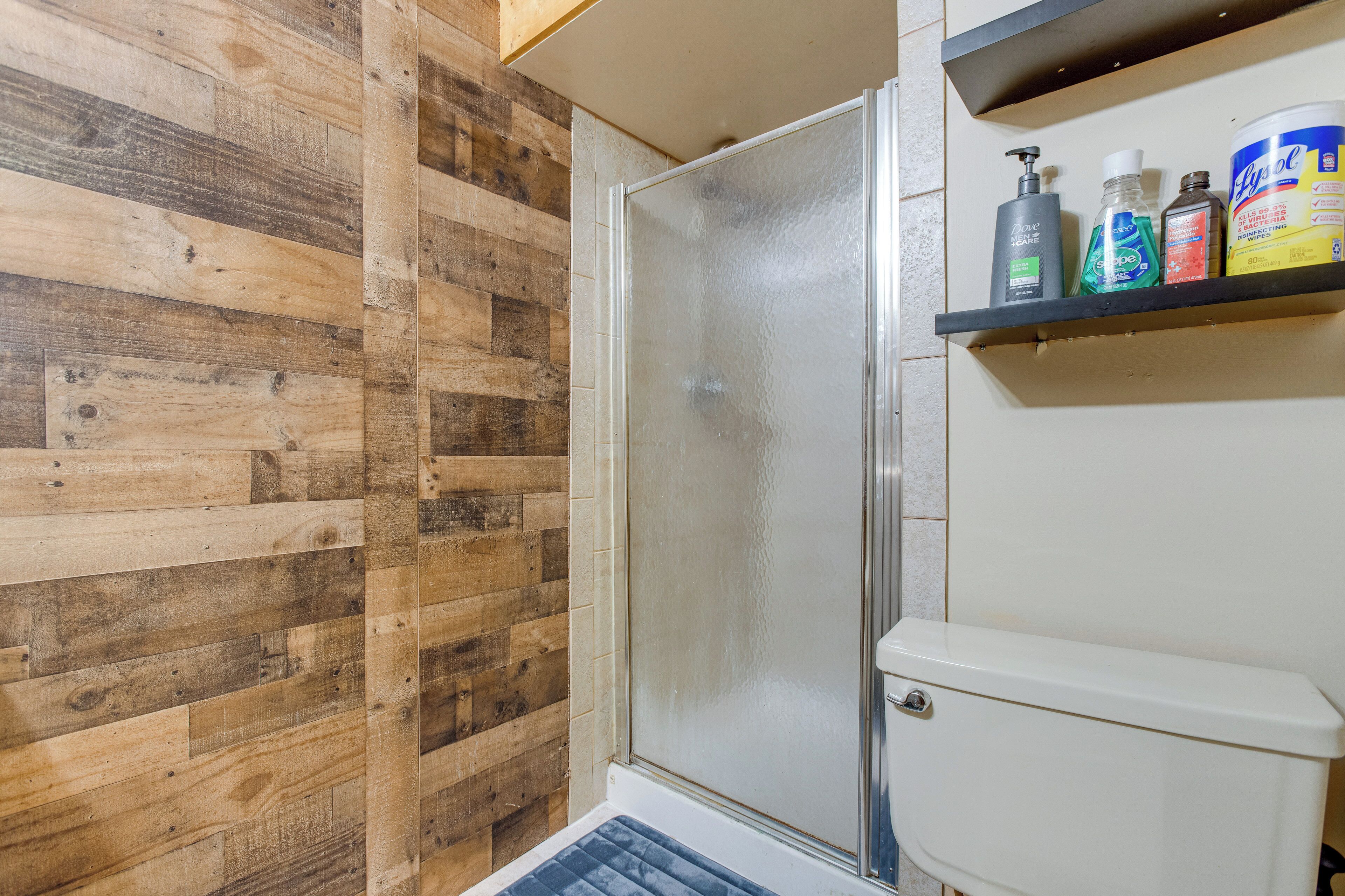 Une salle de bain avec un mur en bois, une cabine de douche en verre et une étagère contenant des articles de toilette.